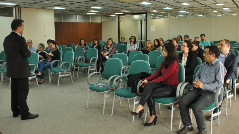 Em uma sala de reuniões, servidores estão sentados às cadeiras e direcionam os olhares com atenção ao diretor-presidente da RS-Prev, em pé, que conversa com os diretores e gestores sobre as novas orientações.
